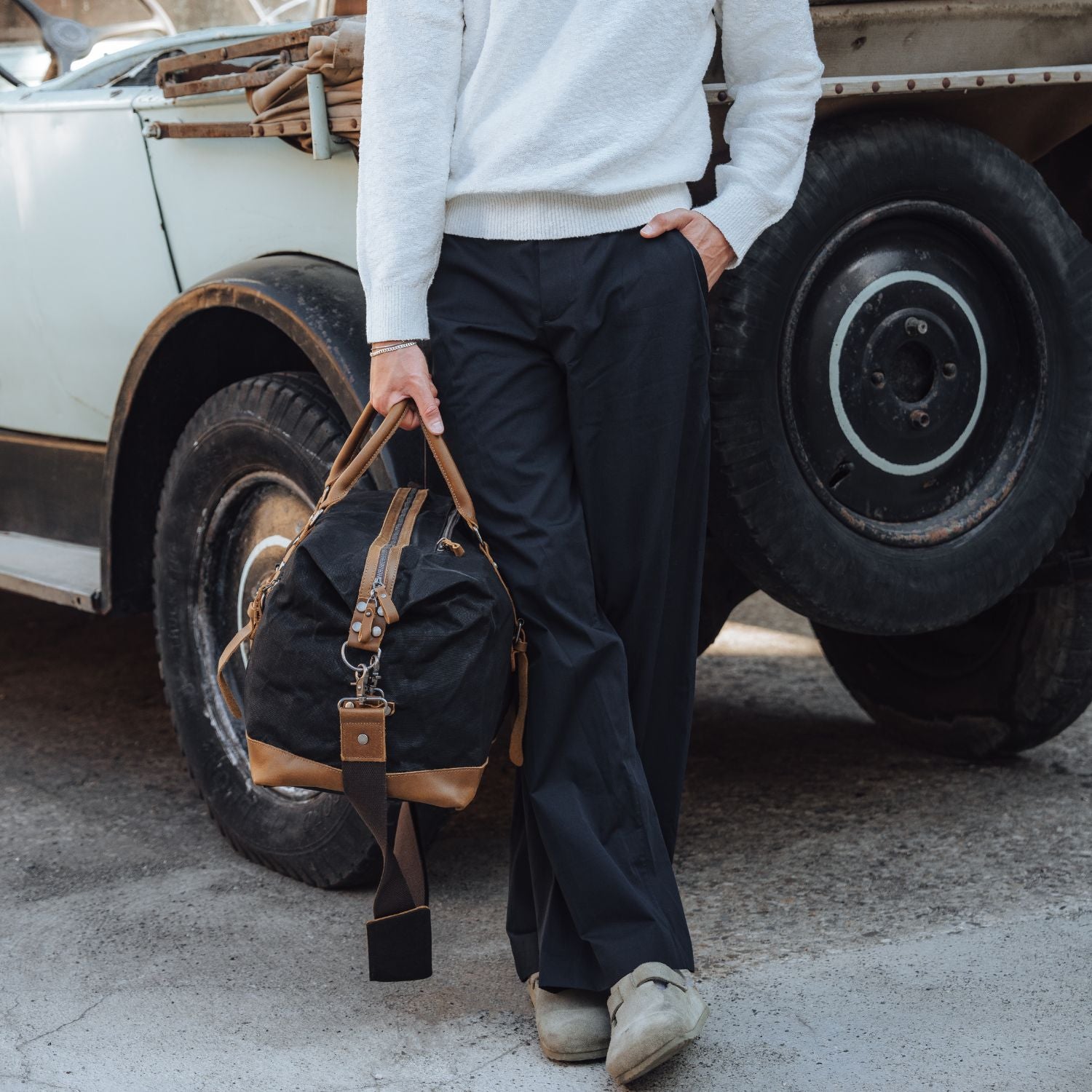 Man leant against a vintage car holding the Humber - Black holdall by his side with the two leather carry handles.
