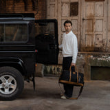 Man opening rear door of Range Rover whilst carrying the Humber - Black waxed cotton canvas and reclaimed leather holdall.