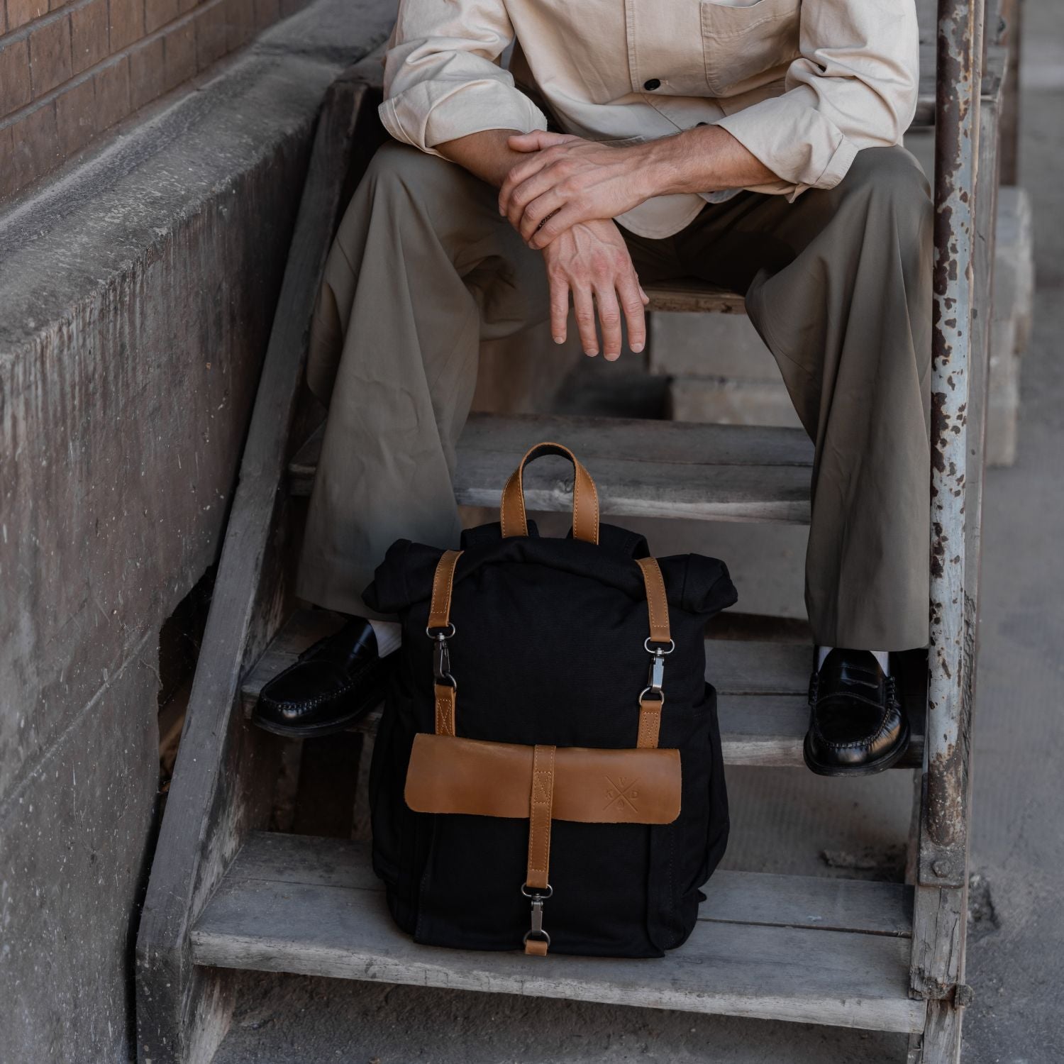 Man sat on steps with the Tay canvas rolltop backpack on the step below.