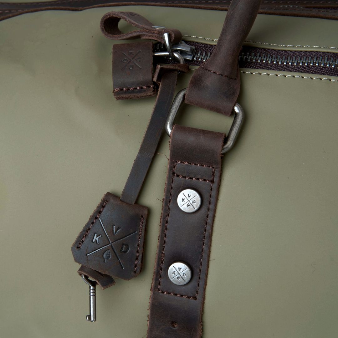 Close-up of a green bag with a brown leather strap and decorative elements.