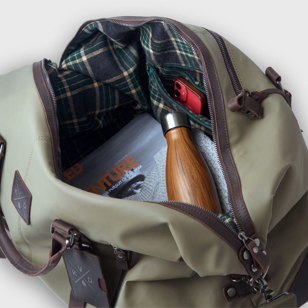 Green duffel bag with plaid lining, phone, and wooden tool on a white background