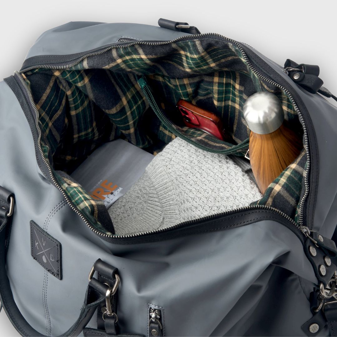 Gray duffel bag with plaid lining, showing a hat and other items inside.