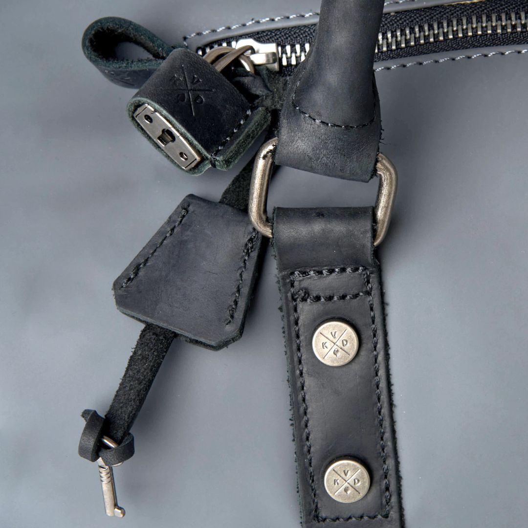 Close-up of a dark gray leather strap with metal hardware on a gray background