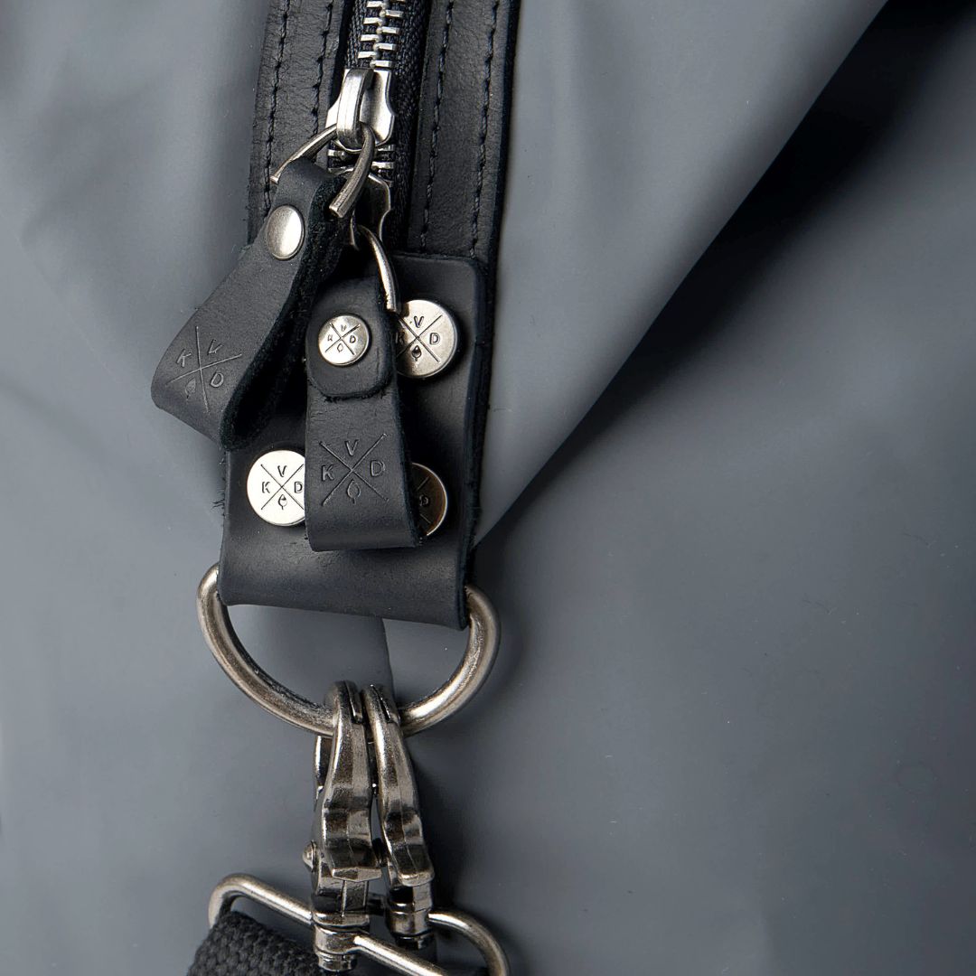 Close-up of a black leather strap with metal hardware on a gray background