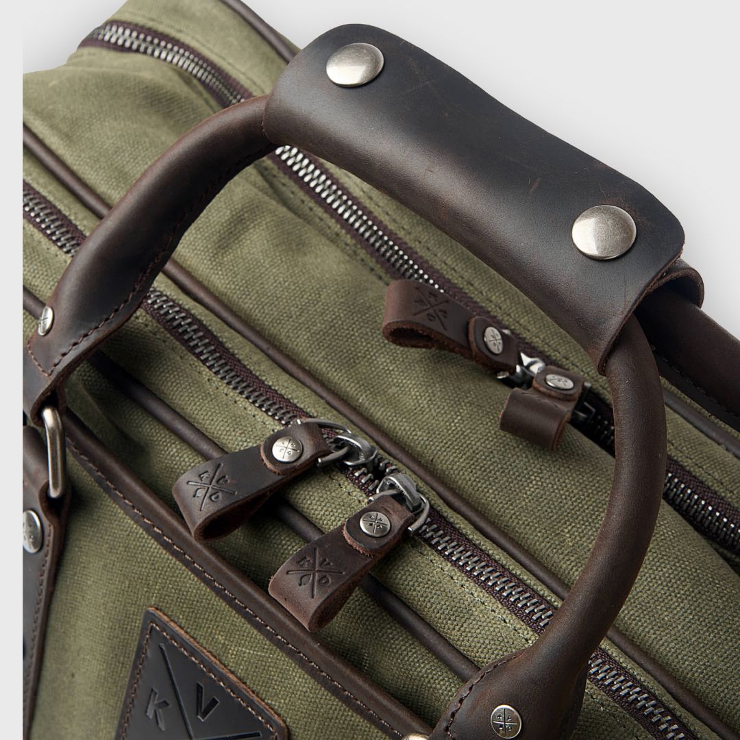 Close-up of a green suitcase with brown leather handles and zippers.