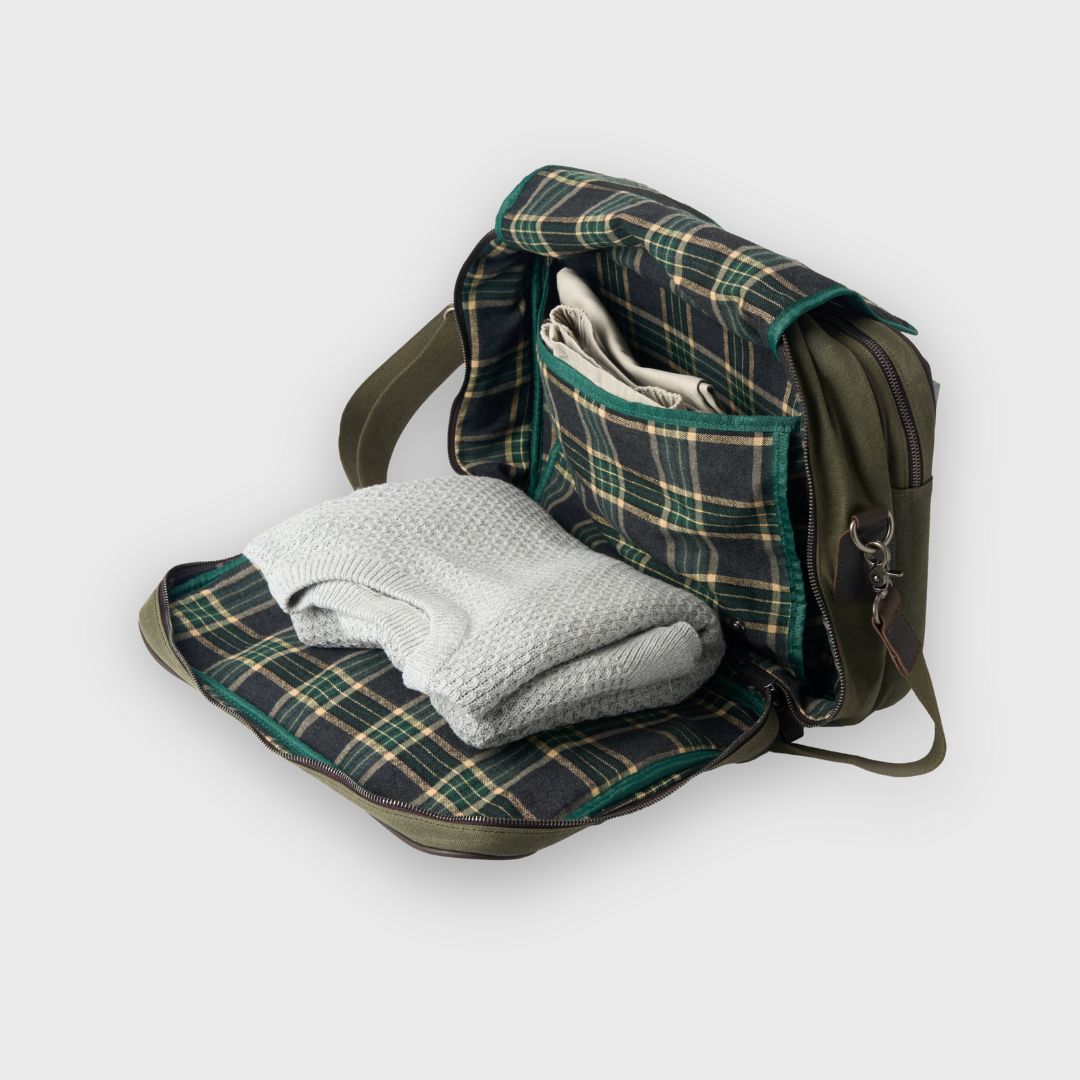 Green plaid blanket folded and placed inside an open green backpack on a white background