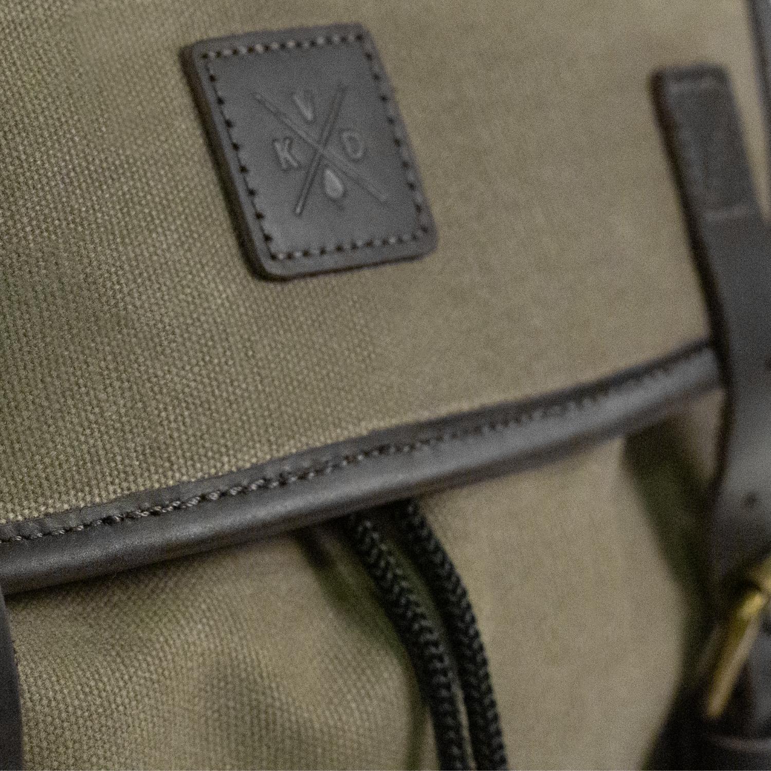 Close up image of dark leather trim and Kovered logo on the Moss Green backpack.