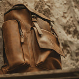 Side image of vintage leather Esk backpack leant against a wall