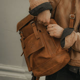 Man unzipping side pocket of reclaimed tan leather backpack 