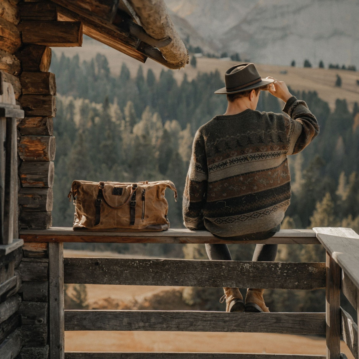 Kovered tan waxed canvas Humber holdall sat on a fence in the Dolomites with a man with a hat on#colour_tan