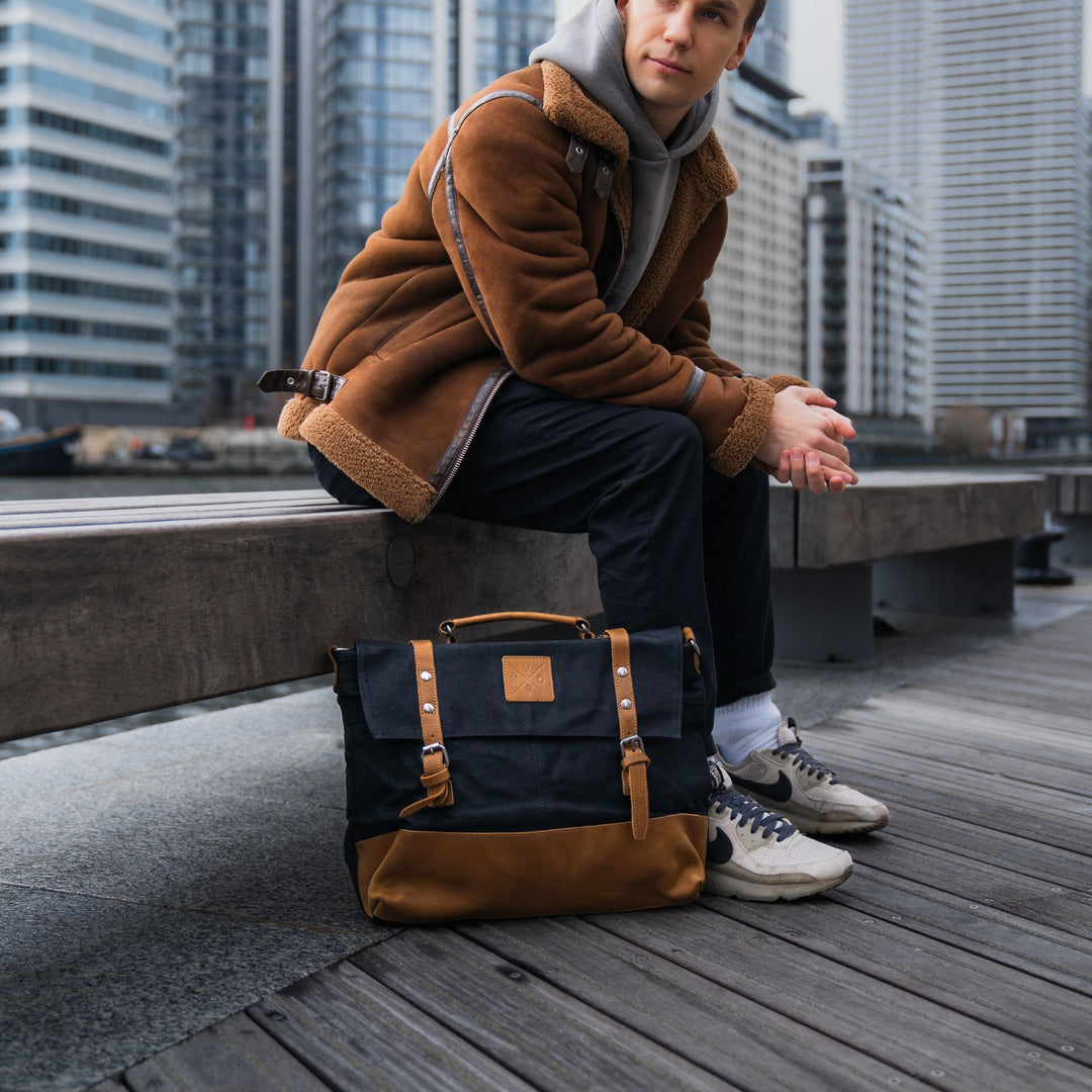 Kovered Mersey messenger bag in black and tan made from waxed canvas and reclaimed leather on the floor in London with model#colour_black