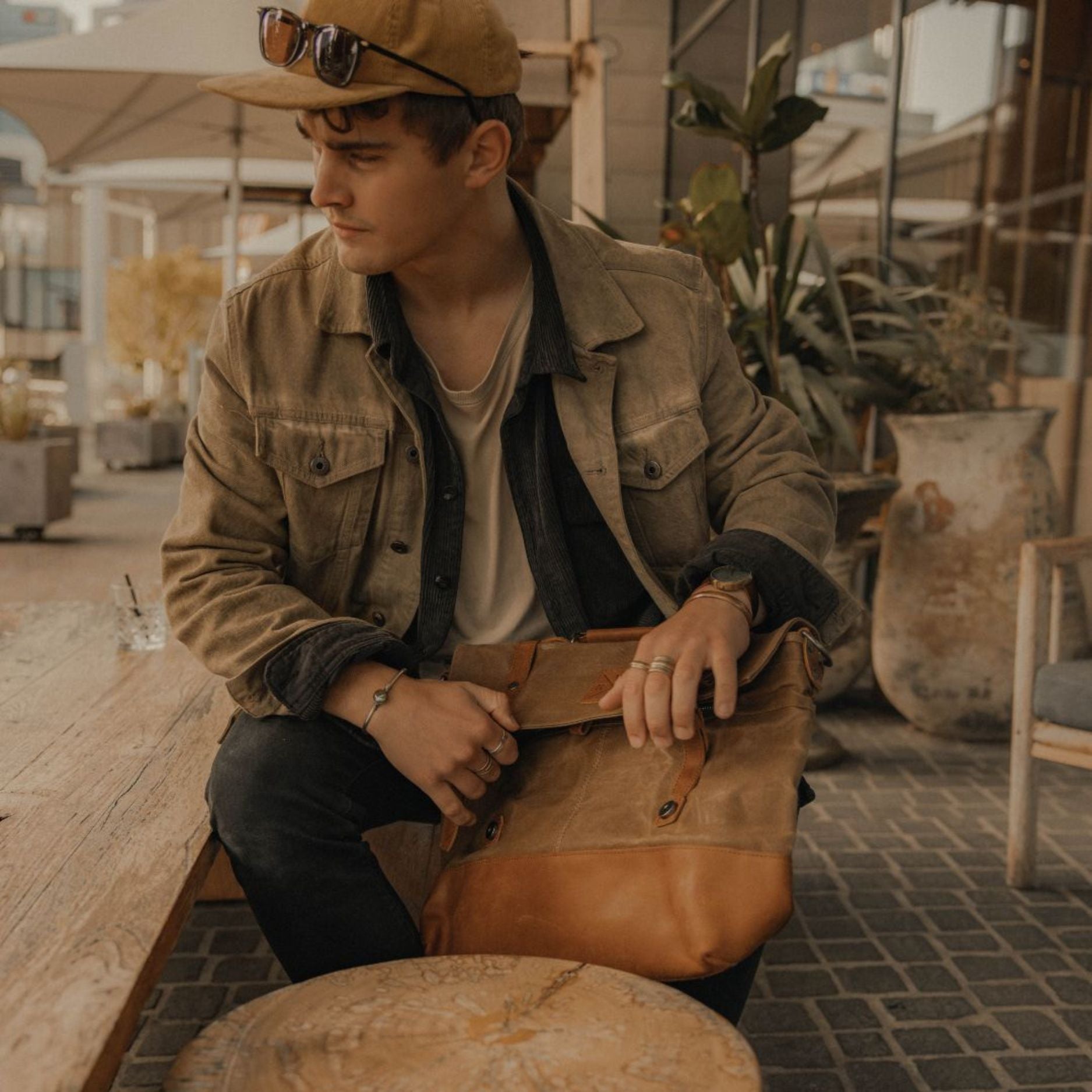 Kovered Mersey messenger laptop bag in brown held by model in coffee shop#colour_tan