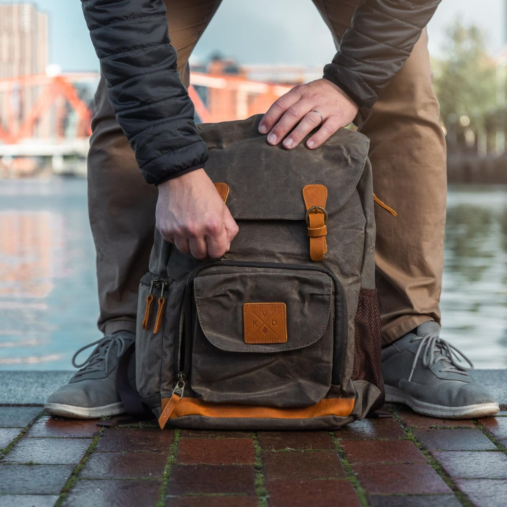 Kovered dark green photography backpack lifestyle photo with model opening the bag using the magnetic buckle by a lake#colour_moss-green