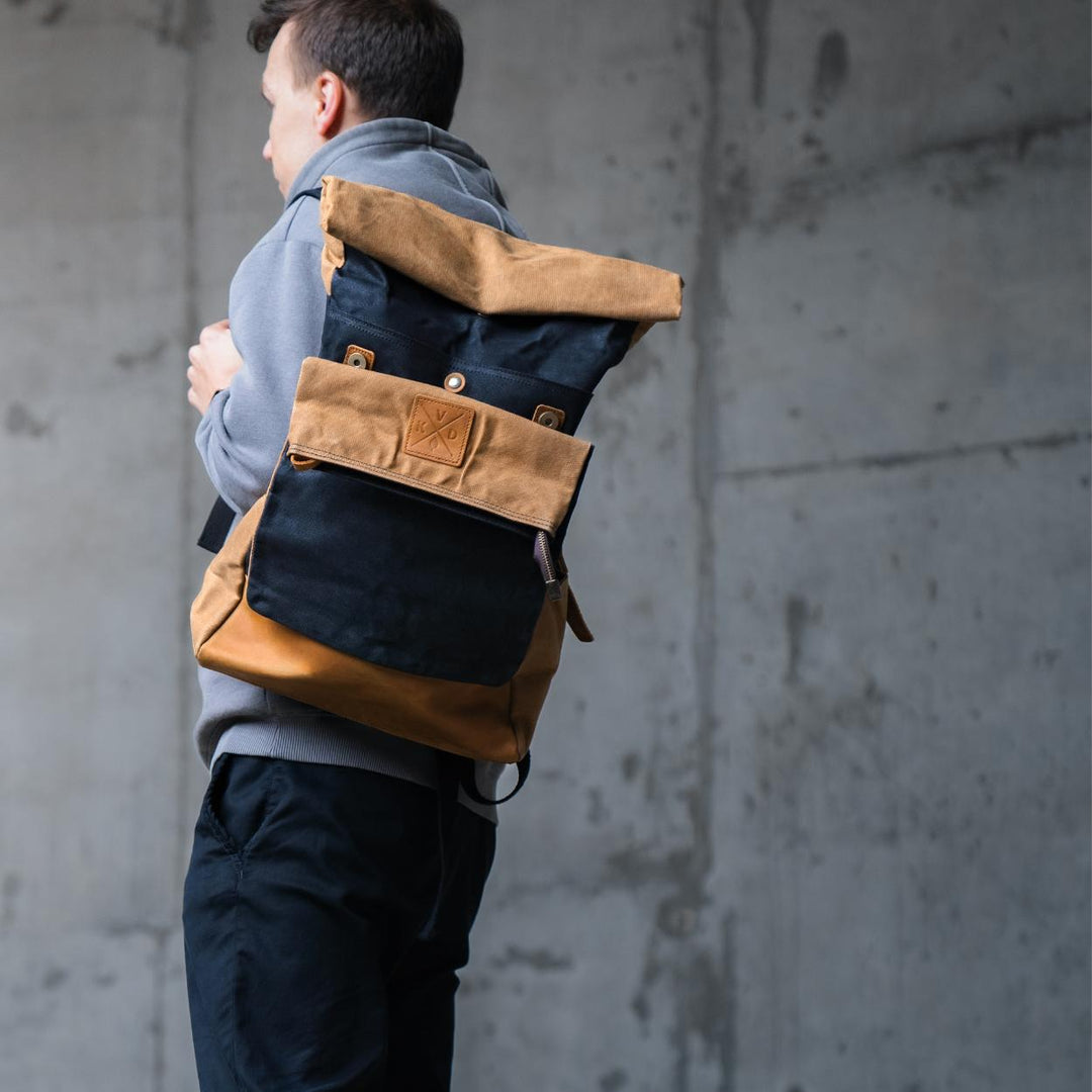 Kovered taw black and tan waxed canvas rolltop backpack being held by a model#colour_black
