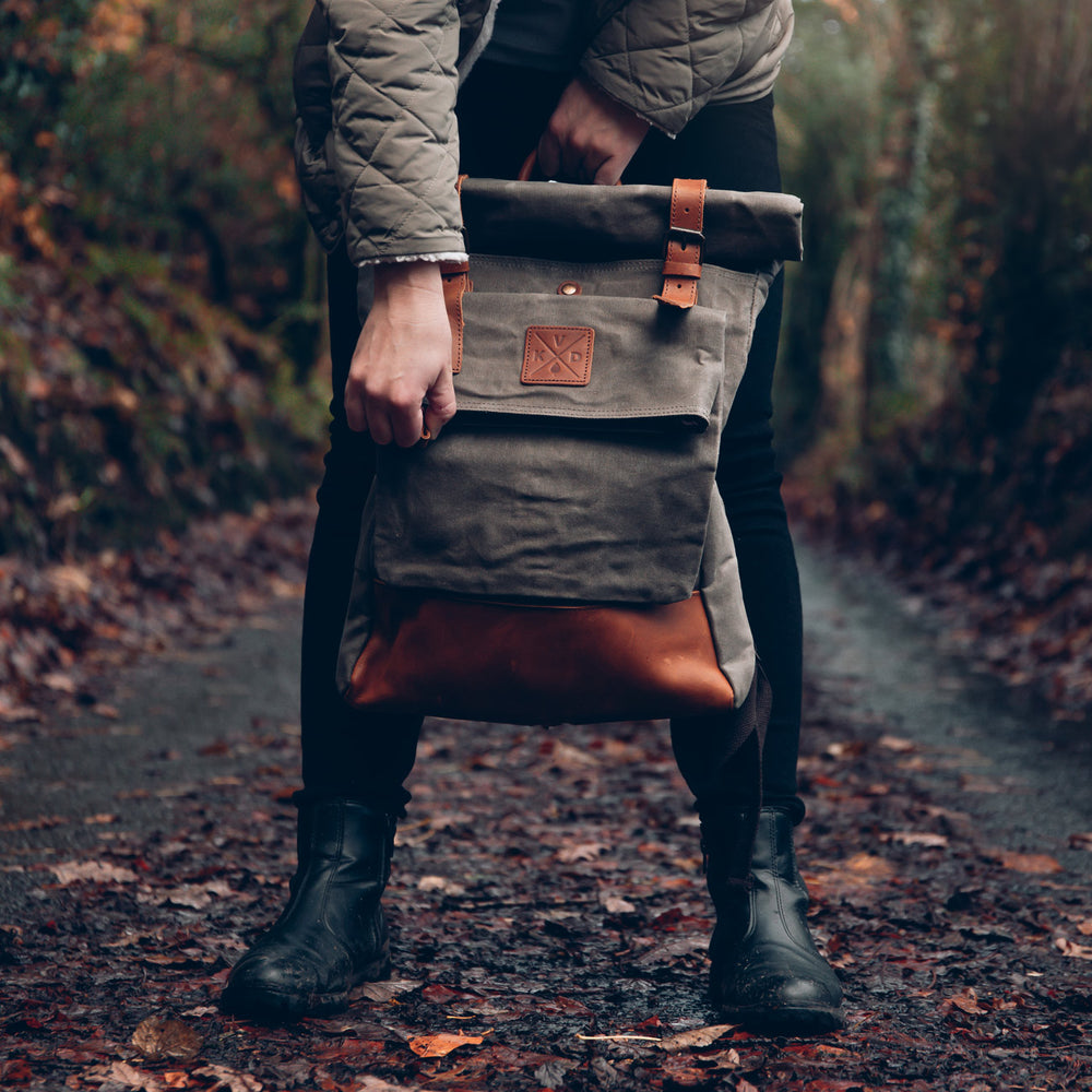 Green rolltop waxed canvas backpack held by model in a forest#colour_moss-green