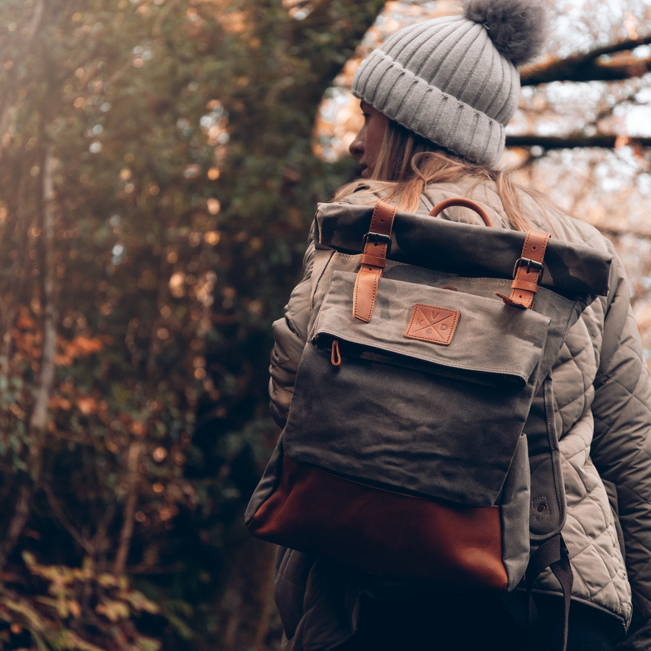 Green waxed canvas rolltop backpack on model wearing a beanie hat#colour_moss-green