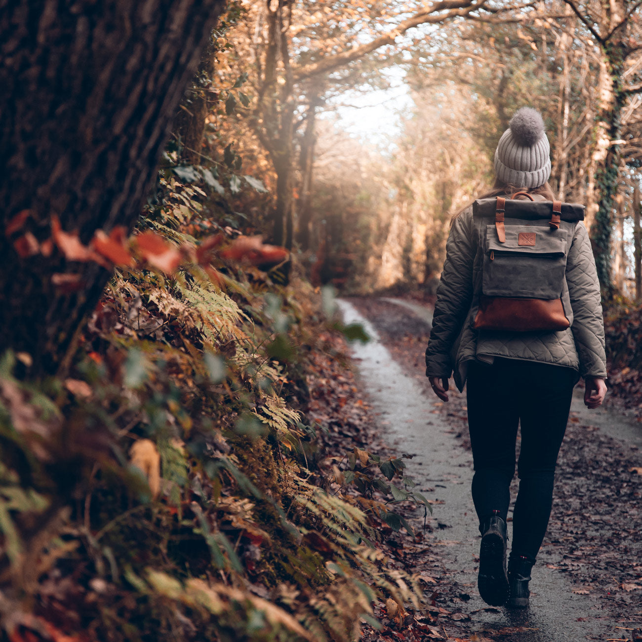 Green rolltop backpack made from waxed canvas on model walking through a forest#colour_moss-green