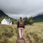 Taw waxed canvas rolltop backpack on model walking through a field#colour_tan