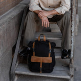 Man sat on steps with the Tay canvas rolltop backpack on the step below.