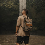 Tay canvas and reclaimed leather backpack on model in front of waterfall in Bali#colour_taupe