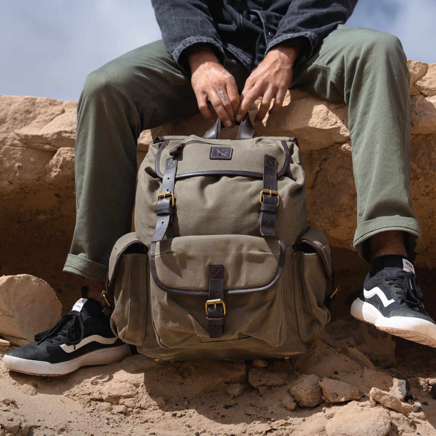 Mat sat resting on a rock holding the Lune Backpack with the leather carry handle
