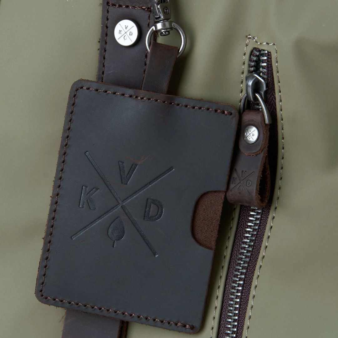Brown leather key pouch with zipper and branding on a green background