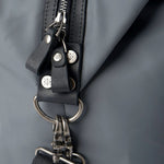 Close-up of a black leather strap with metal hardware on a gray background