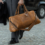 Man carrying a brown leather weekend holdall bag through the street