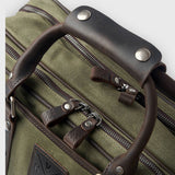 Close-up of a green suitcase with brown leather handles and zippers.