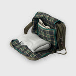 Green plaid blanket folded and placed inside an open green backpack on a white background