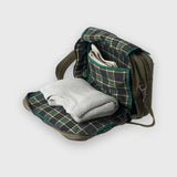 Green plaid blanket folded and placed inside an open green backpack on a white background