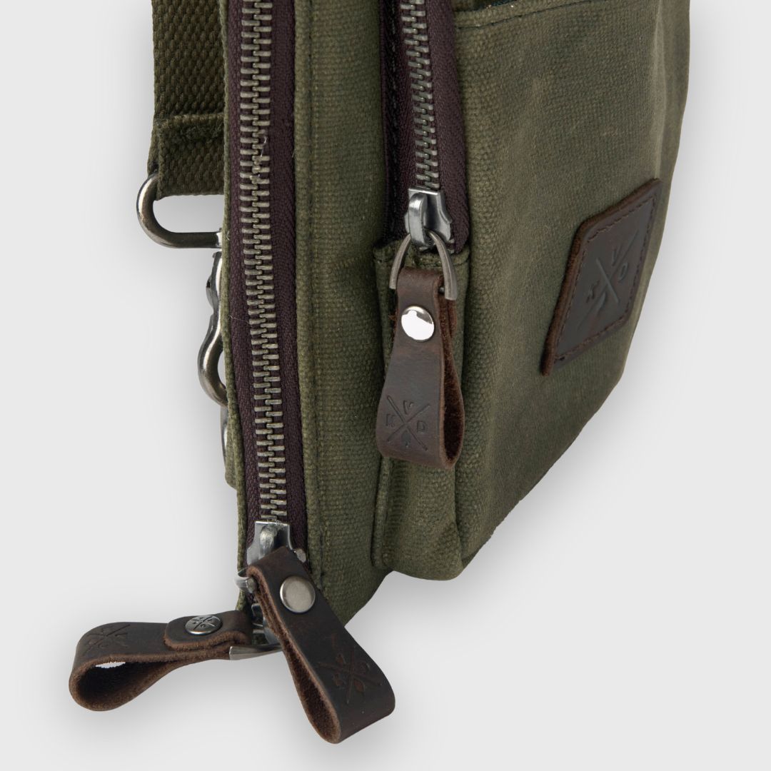 Green canvas bag with brown leather zippers on a white background