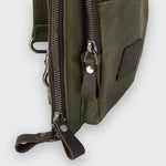 Green canvas bag with brown leather zippers on a white background