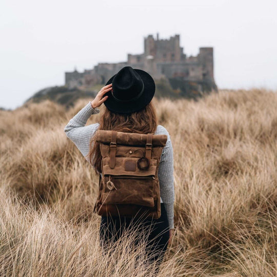 Kovered Taw tan waxed canvas rolltop backpack on a female model stood in a field in front of a castle#colour_tan